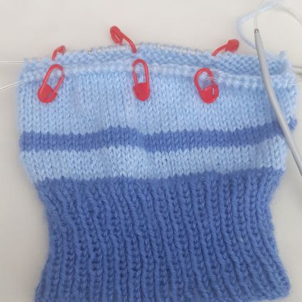 image showing body section of knitted baby beanie done on circulars completed showing stitch marker placement